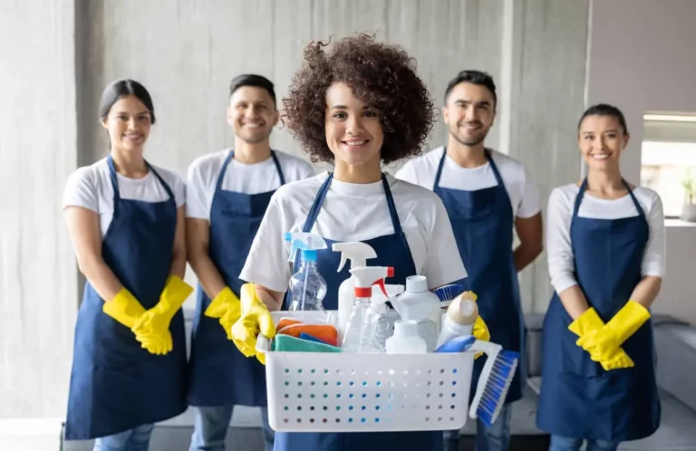 Diverse cleaning team smiling with supplies in office.