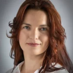 Woman with auburn hair, white shirt, neutral background.